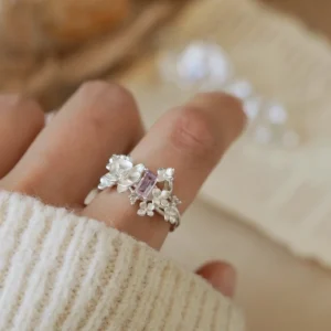 Close-up of a hand wearing the Unique Gemstone Ring, an orchid-inspired S925 silver ring with a central purple gemstone.