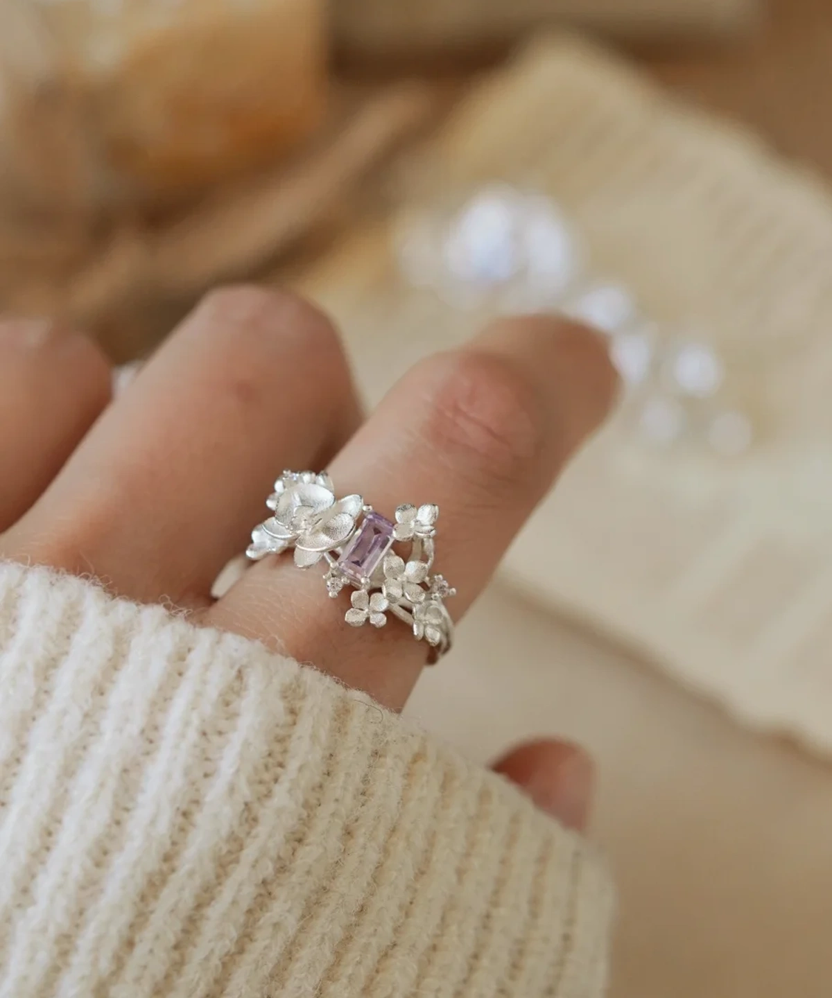 Close-up of a hand wearing the Unique Gemstone Ring, an orchid-inspired S925 silver ring with a central purple gemstone.