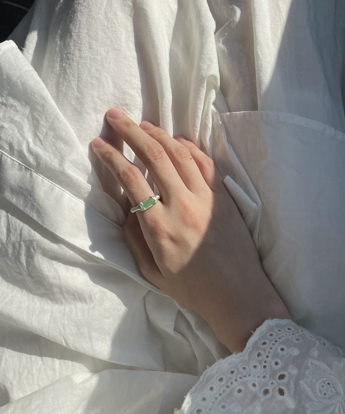 A hand wearing a Custom Couple Ring in S925 silver, featuring a natural light green tourmaline gemstone in an organic setting.