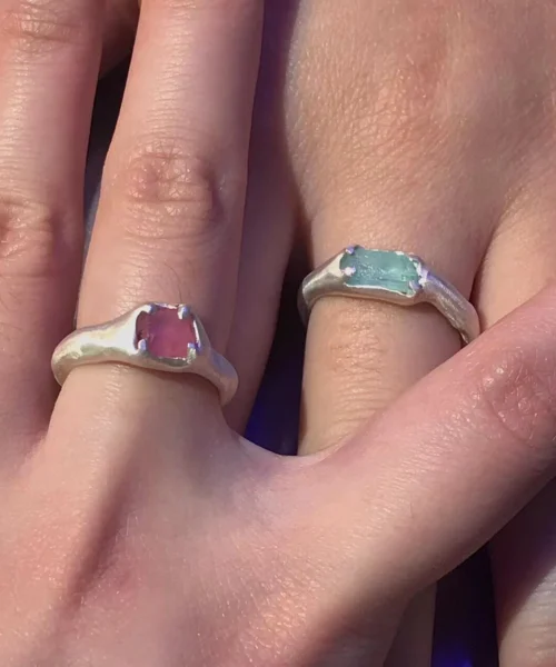 Two hands wearing matching Custom Couple Rings in S925 silver, set with raw pink and blue natural tourmaline gemstones.