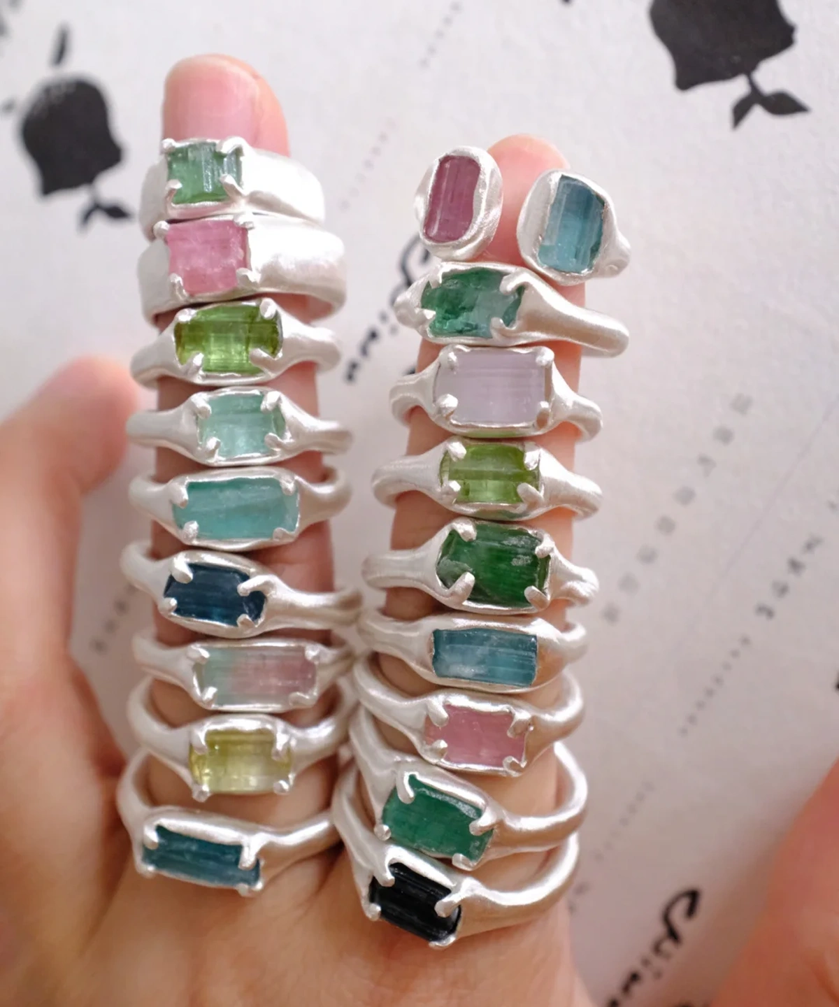 Close-up of stacked Custom Couple Rings in S925 silver, featuring natural multi-color tourmaline gemstones with organic handcrafted settings, held in fingers.
