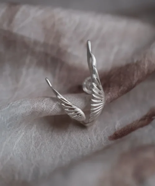 Close-up of a Dual Wing Earring in S925 sterling silver, highlighting the intricate, sculpted wing details on a soft fabric background.