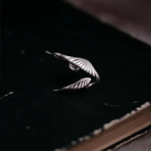 A single Dual Wing Earring in S925 sterling silver, showcasing its unique double-wing design, placed on a dark vintage book.