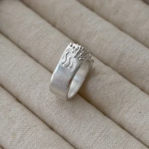 999 fine silver wide band ring on linen, side angle showing shell texture transitioning to smooth band