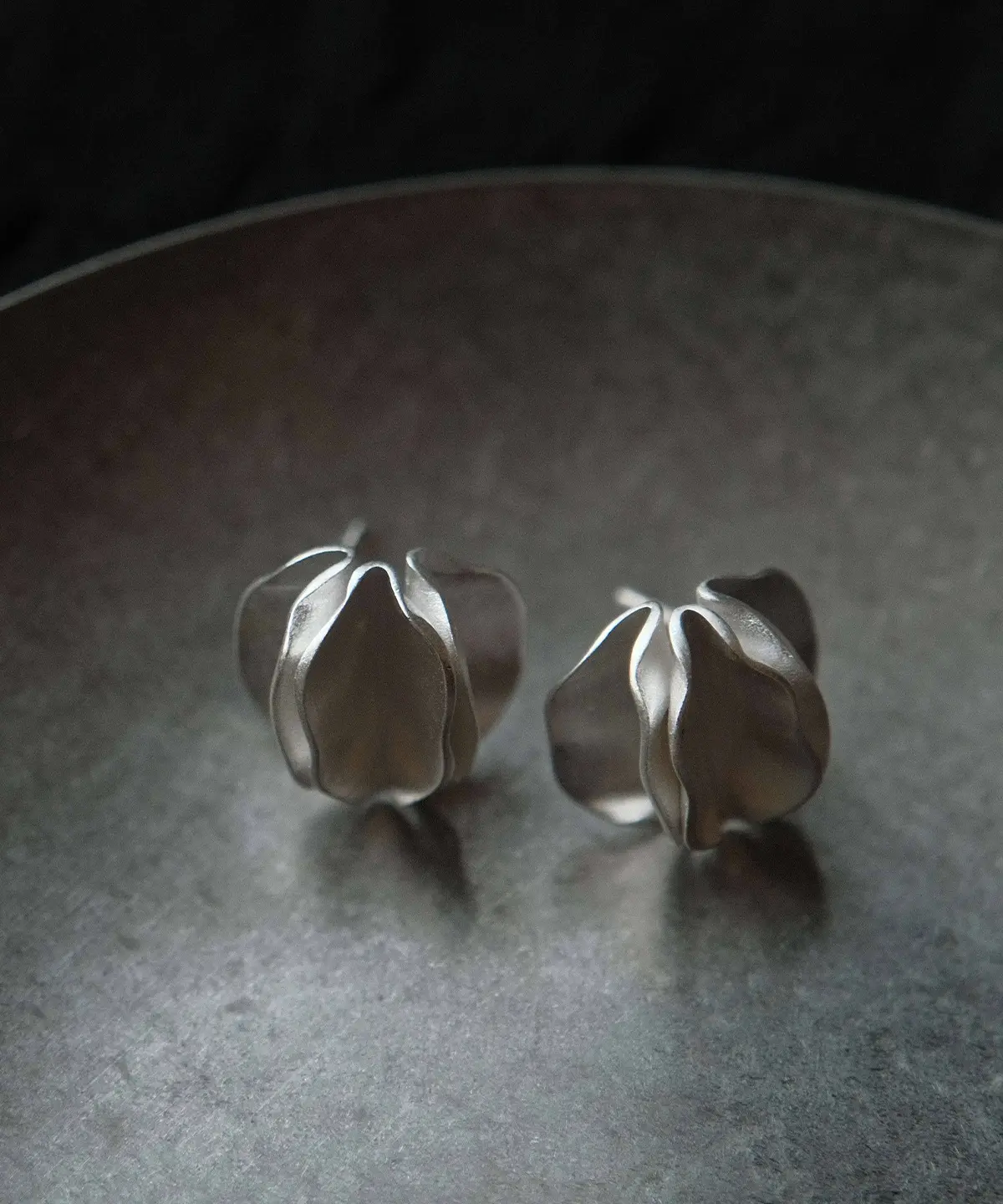 Sterling Silver Stud Earrings – Dark Background Pair Shot pair of sterling silver stud earrings on dark tray, sculptural handmade silver jewelry