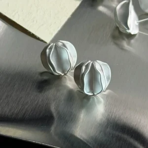 multiple sterling silver stud earrings on metal surface with flowers, handmade jewelry display
