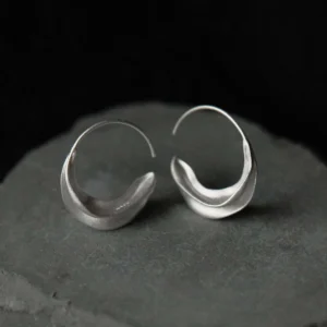 silver crescent moon earrings resting on dark stone, showing curved hoop