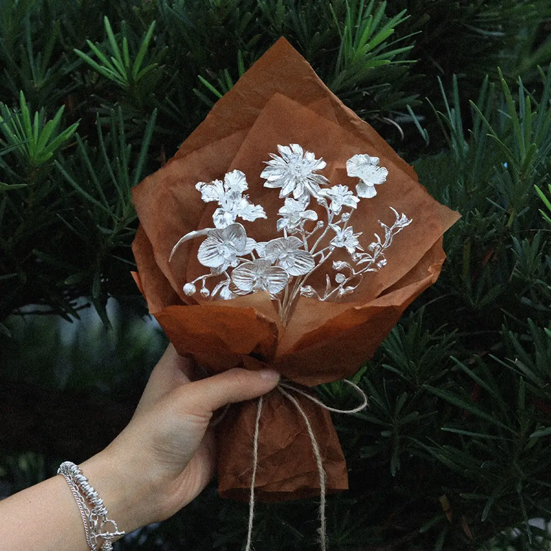 Handmade pure silver flower bouquet held by hand, wrapped in brown paper as a lasting artisan jewelry gift.