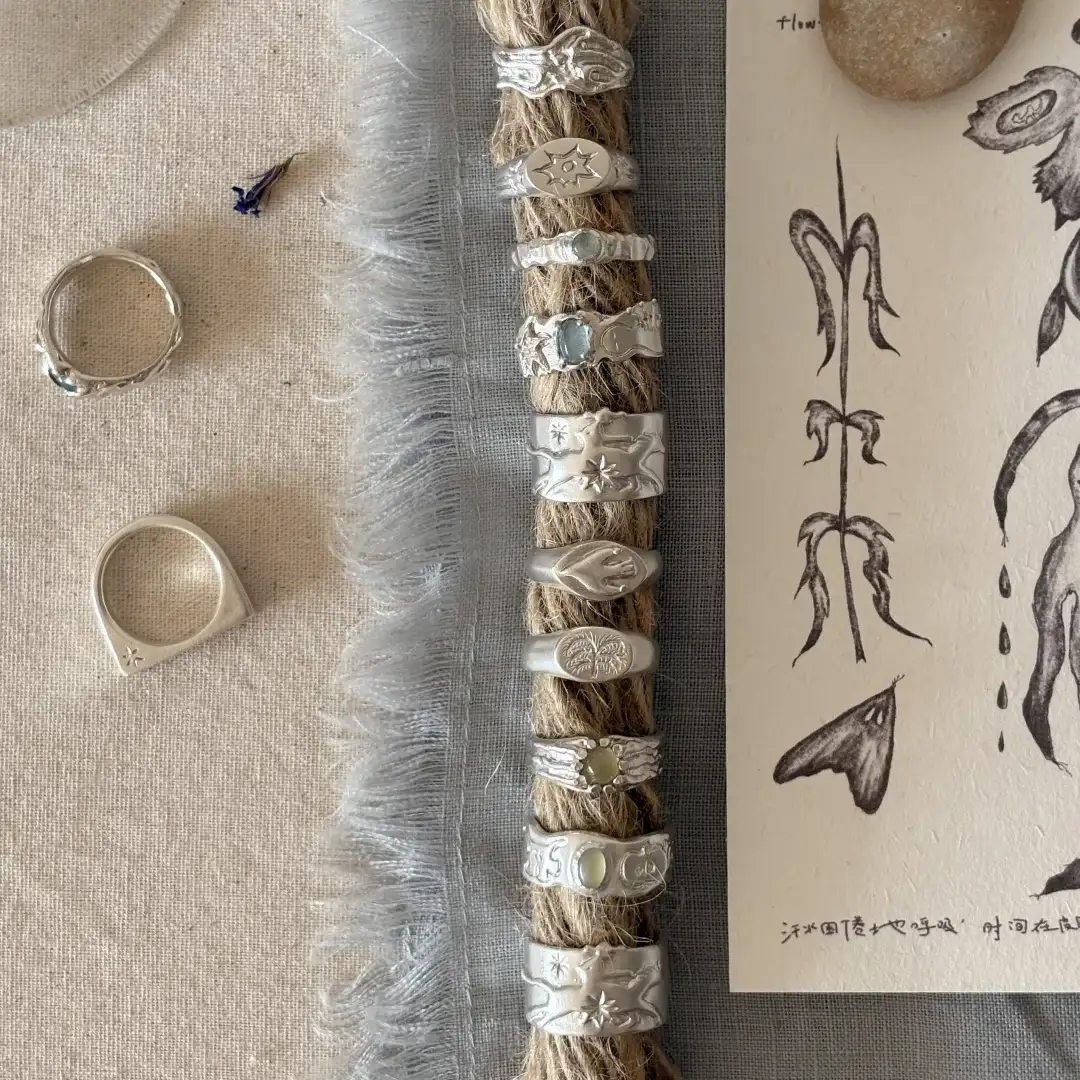 Silver rings placed beside fabric, rope, and hand-drawn design sketches, showing finished artisan jewelry with its visual references.