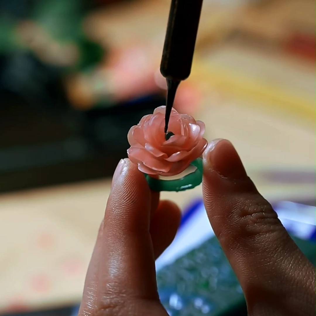 Hands shaping a pink and green wax flower ring model, adding small details before the piece is cast into silver.