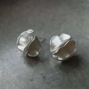 pair of handmade silver stud earrings on ceramic dish, round sculptural design