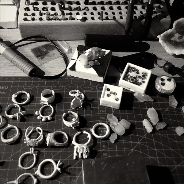 Blogs 1 Unfinished silver ring settings and loose gemstones on a jewelry workbench, waiting to be set and finished by hand.