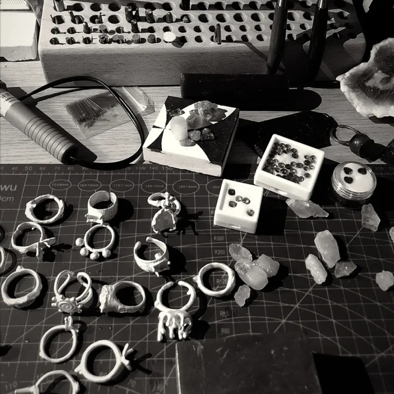 Unfinished silver ring settings and loose gemstones on a jewelry workbench, waiting to be set and finished by hand.
