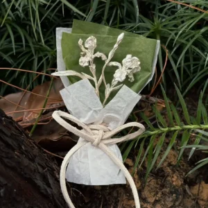 Miniature iris bouquet in 950 silver with green paper wrap displayed among wet garden leaves