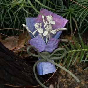 Handmade miniature silver flower bouquet with purple paper wrap in a rain-darkened garden