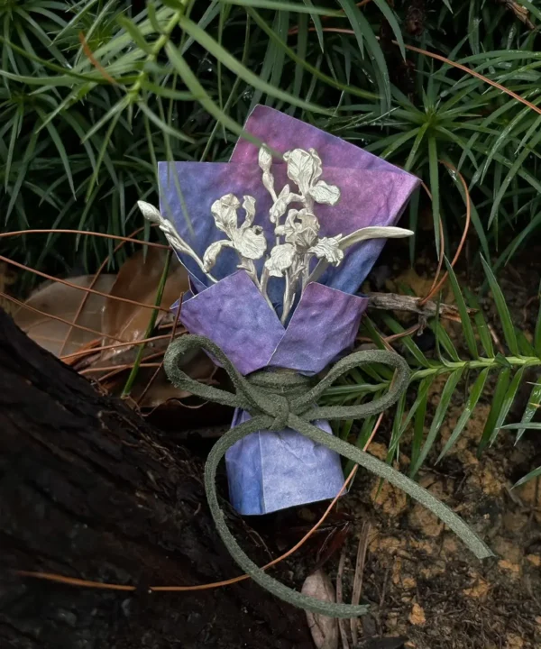 Handmade miniature silver flower bouquet with purple paper wrap in a rain-darkened garden