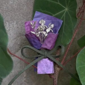 5.5 g miniature silver iris bouquet in purple wrapping beside a broad green leaf