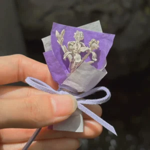 Hand holding a purple wrapped 5.5 g miniature silver iris bouquet outdoors