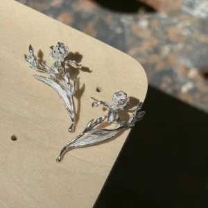 Bud and leaf silver iris flower earrings shown flat as a pair on a pale board