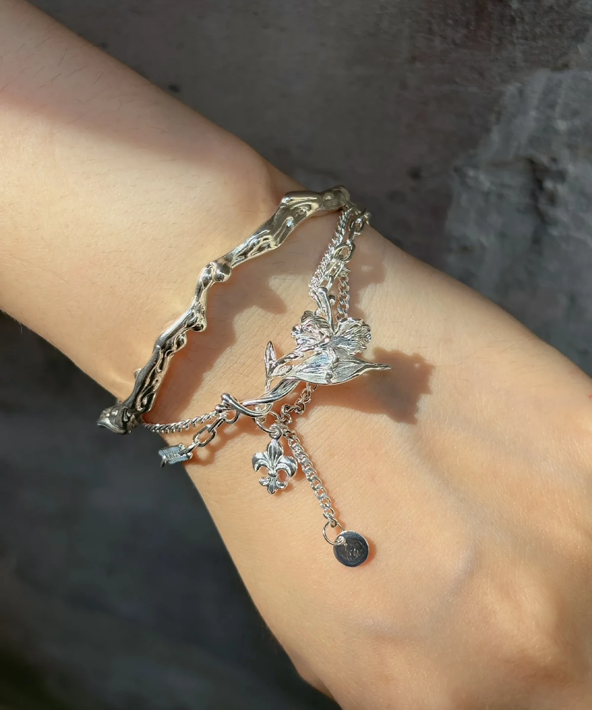 Iris bracelet worn across the wrist with a sculpted silver flower and dangling emblems