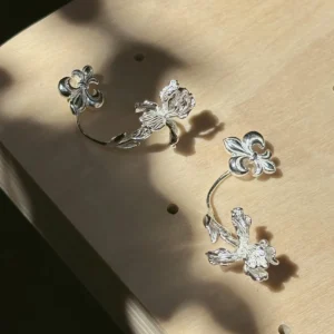 Sterling silver iris ear jacket earrings with fleur-de-lis studs and long floral jackets on a warm display board