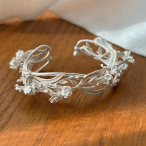 Open cuff bracelet in silver formed from intertwined iris stems, leaves, buds, and flowers