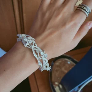 Silver open cuff bracelet with iris flowers and leaves worn beside a table