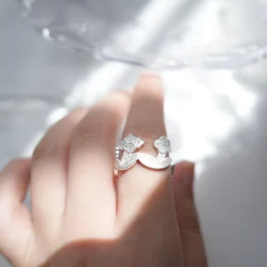 Adjustable silver flower ring worn on the finger, caught in window light