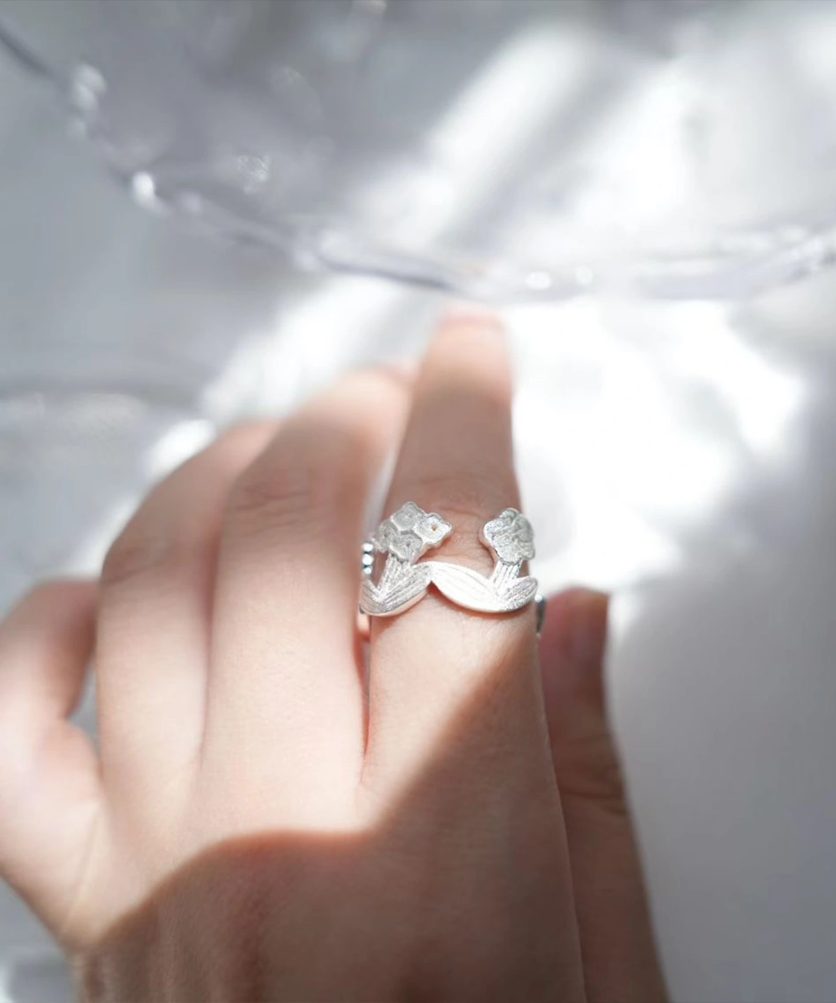 Adjustable silver flower ring worn on the finger, caught in window light