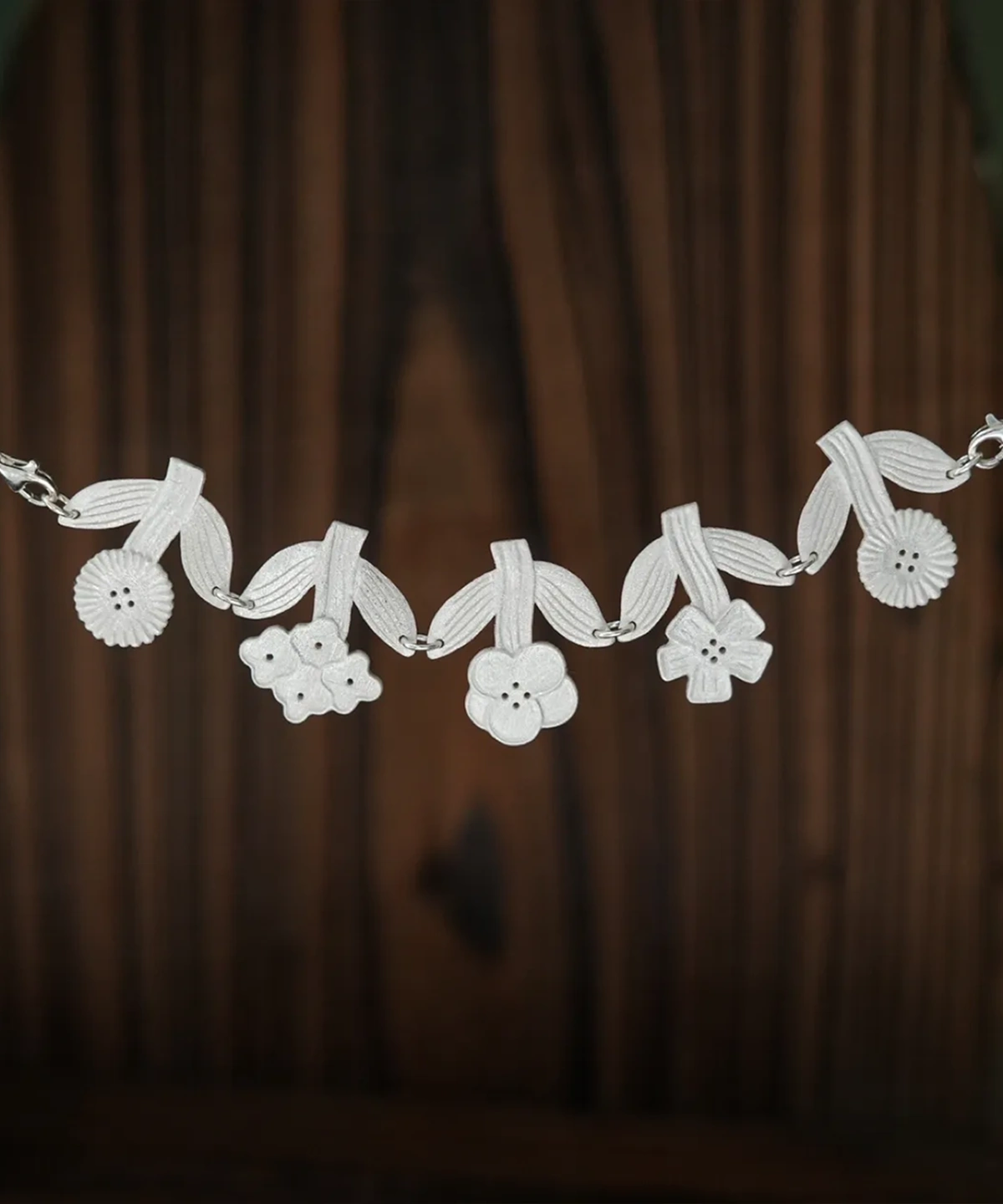 Sterling silver flower necklace laid flat on dark wood, five linked blooms hanging from ribbed leaves