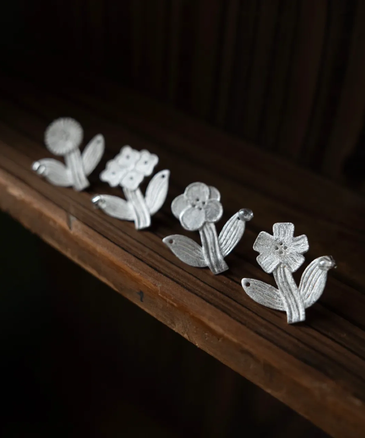 earring-designs-brushed-silver.webpFour flower stud earring designs in brushed sterling silver on dark wood