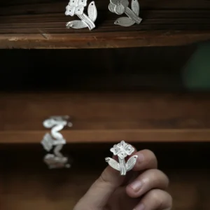 Flower stud earrings in sterling silver displayed on a dark wooden shelf