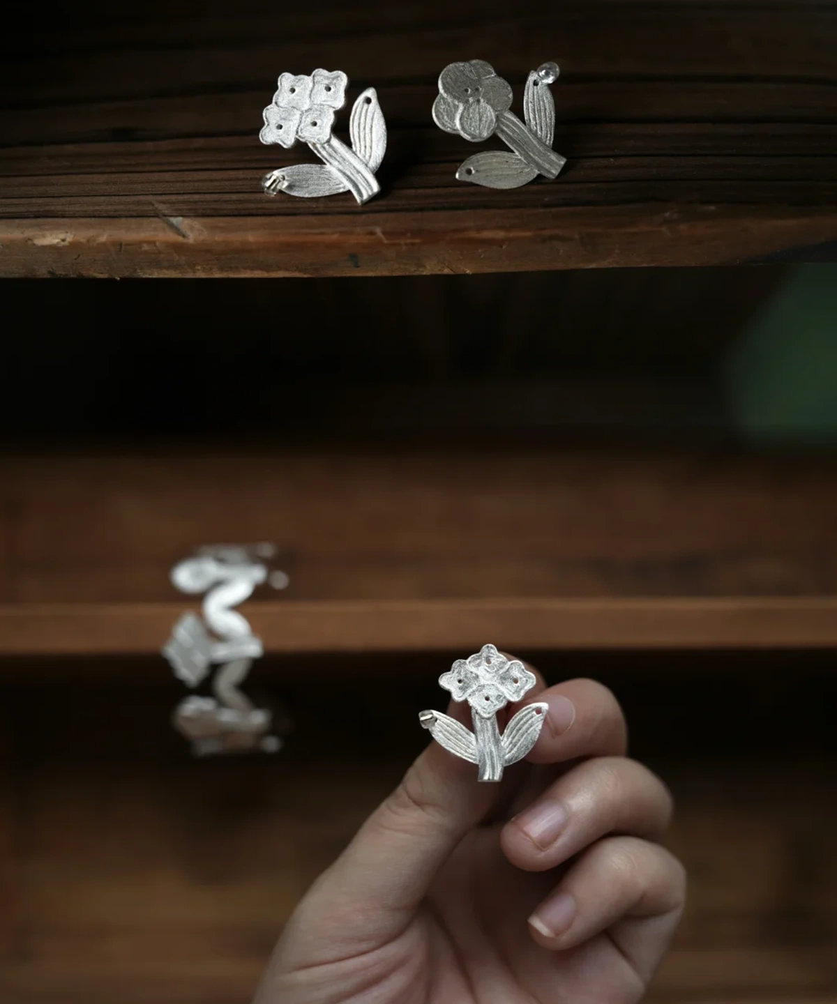 Flower stud earrings in sterling silver displayed on a dark wooden shelf