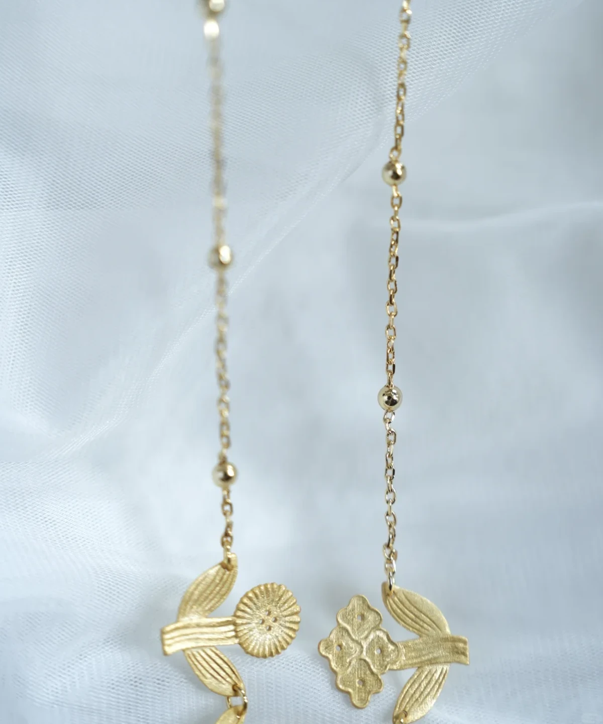 Detail of the gold flower necklace — beaded chains ending in a round bloom and a four-bloom cluster with leaves