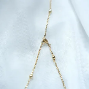 Close-up of the gold flower necklace beaded chain and lobster clasp on white fabric