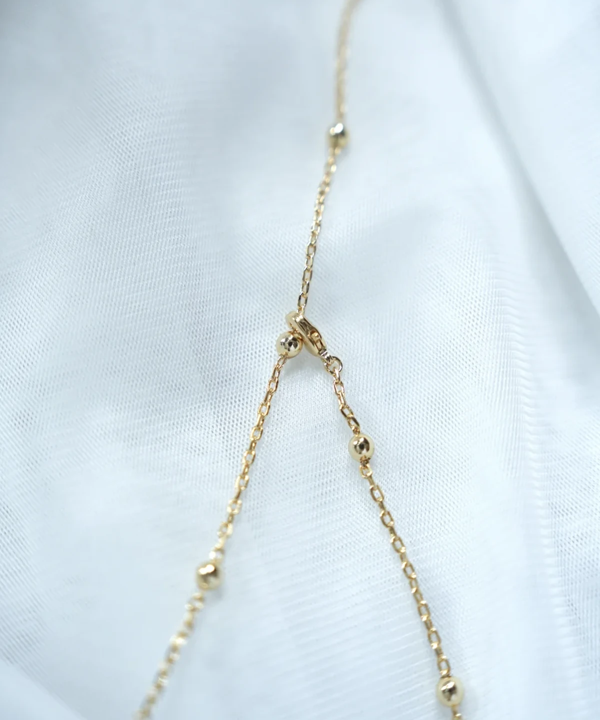 Close-up of the gold flower necklace beaded chain and lobster clasp on white fabric
