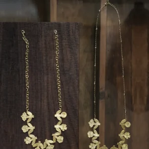 Gold flower necklaces in two lengths hanging on dark wood — short chain and long beaded chain, same linked garland