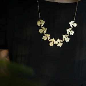 Long gold flower necklace worn over a black top — garland of small blooms and ribbed leaves