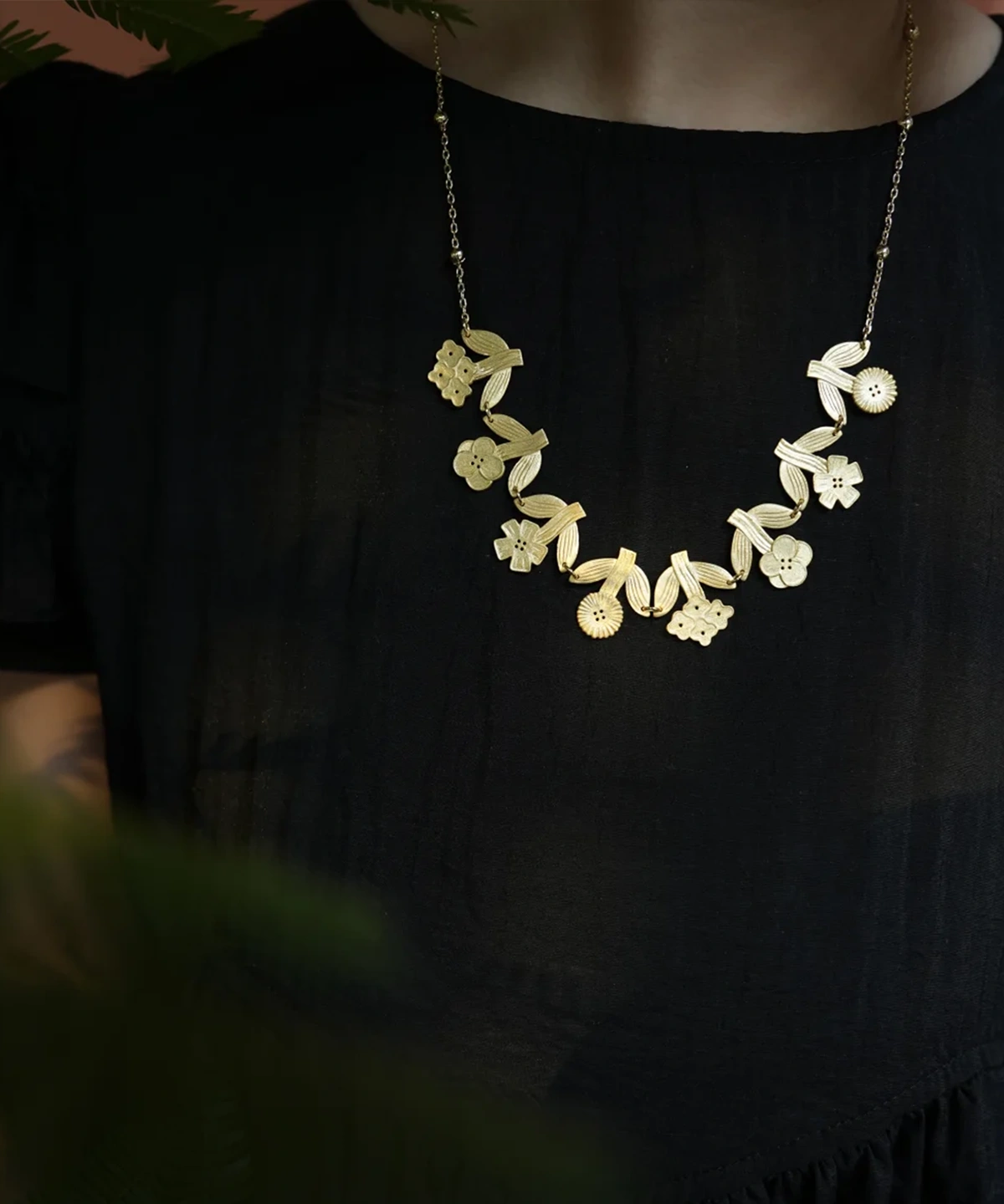 Long gold flower necklace worn over a black top — garland of small blooms and ribbed leaves