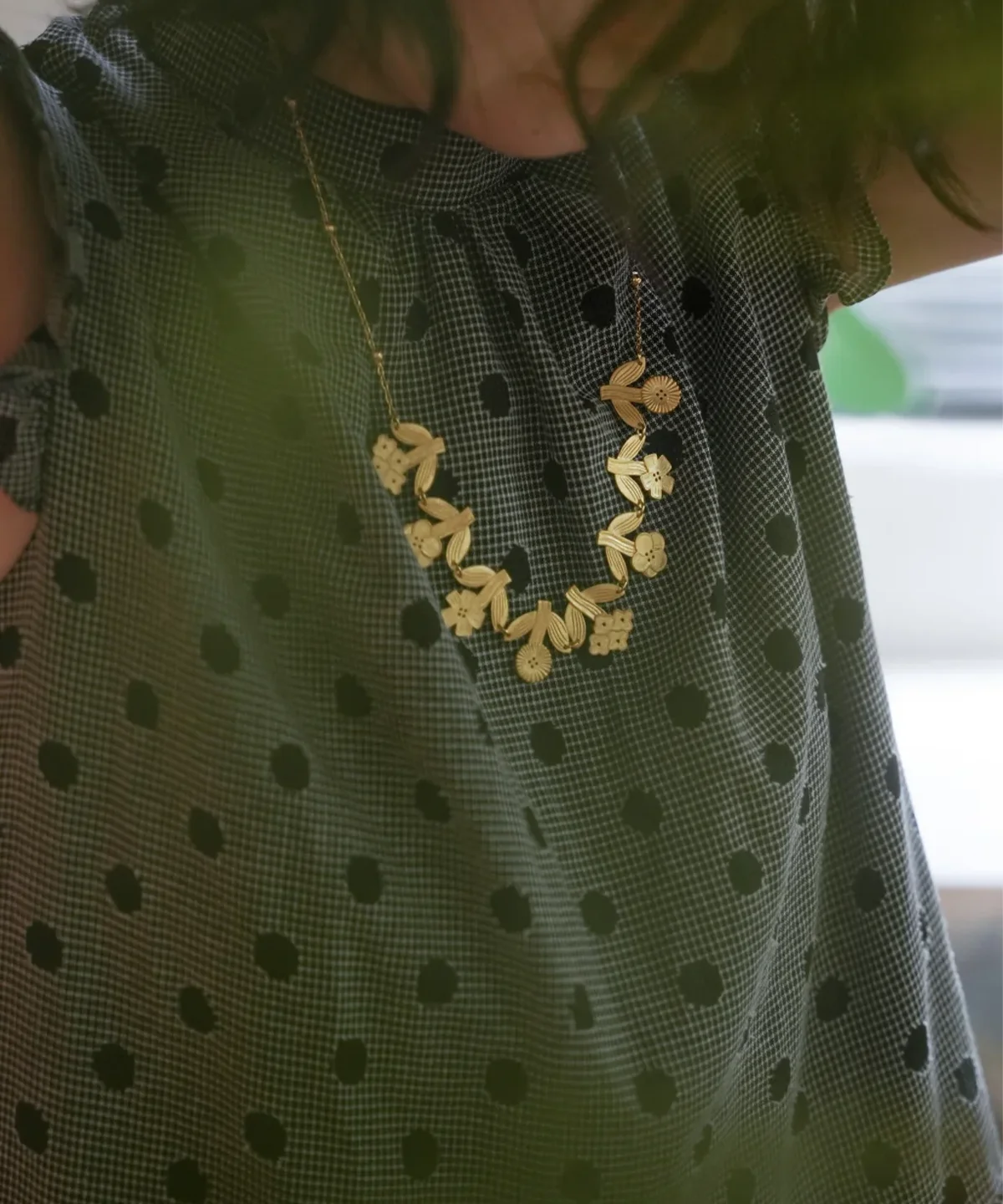 Gold flower necklace worn with a dotted green blouse, garland resting below the collar