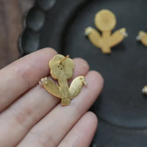 Back of a gold flower stud earring held in hand, showing the post and brushed surface