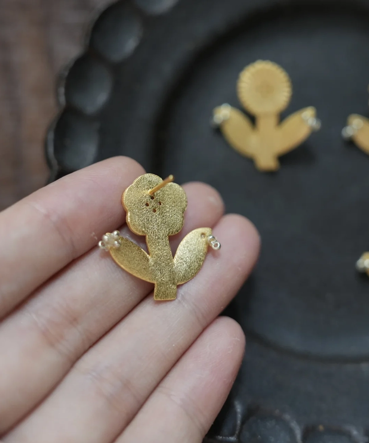 Back of a gold flower stud earring held in hand, showing the post and brushed surface