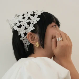 Gold flower stud earring worn with a white lace flower headband and a silver flower ring