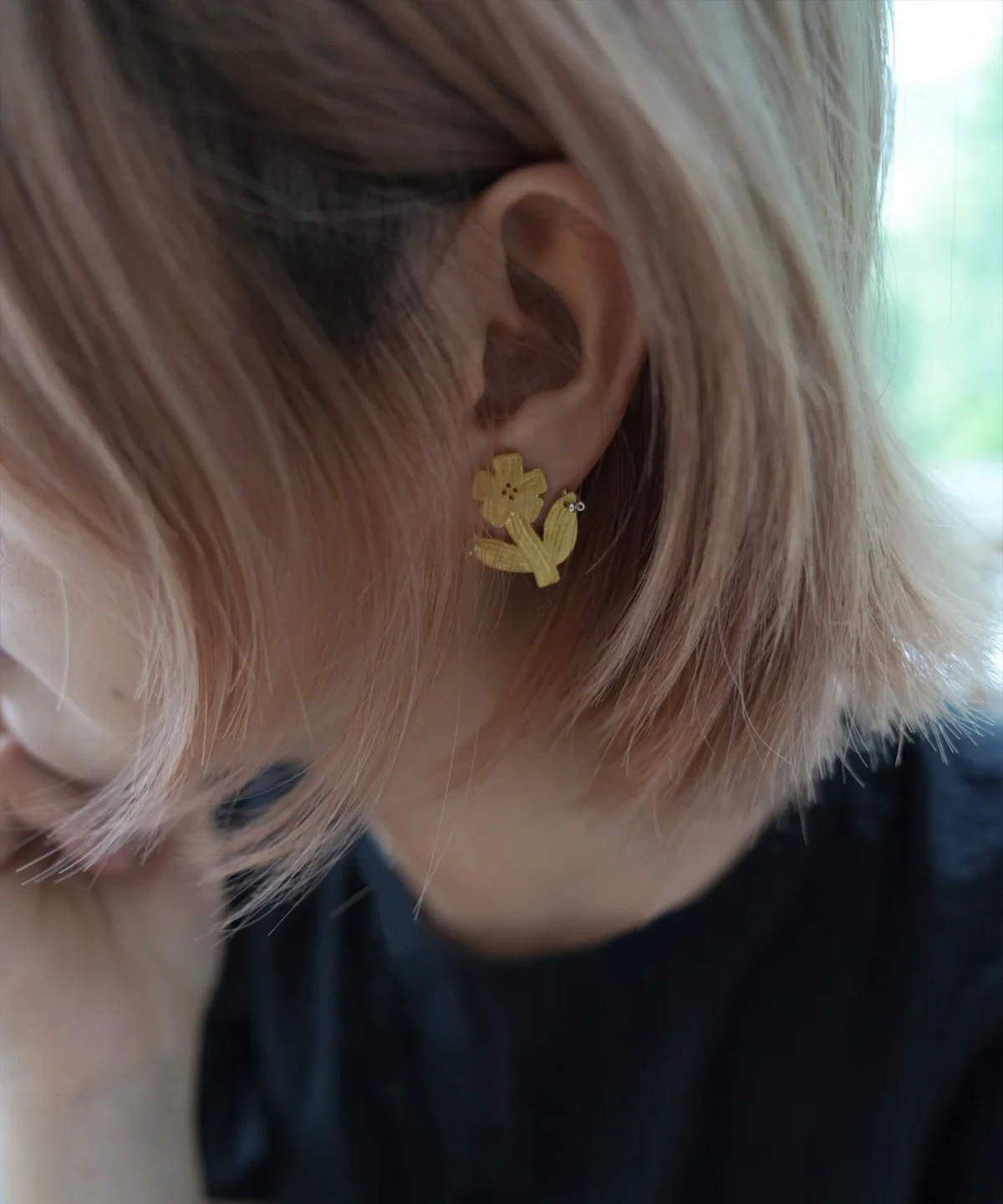 Gold flower stud earring worn on the ear, whole flower with stem and leaf