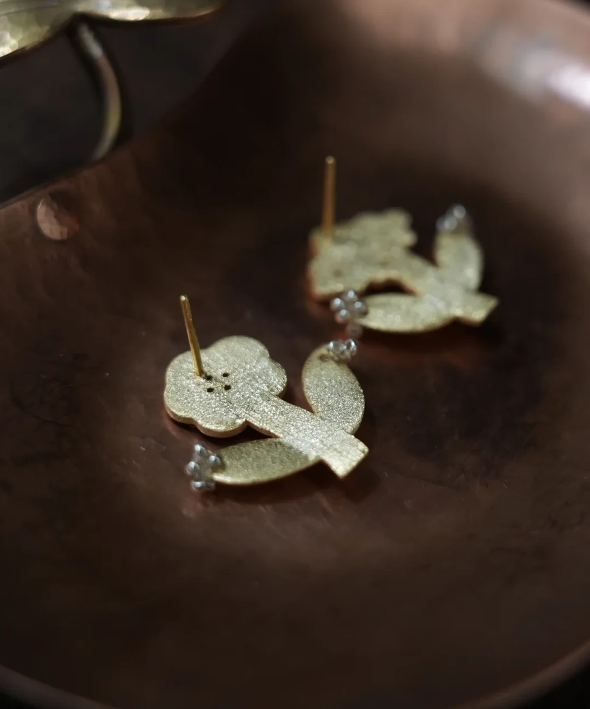 Backs of two gold flower stud earrings resting in a copper dish