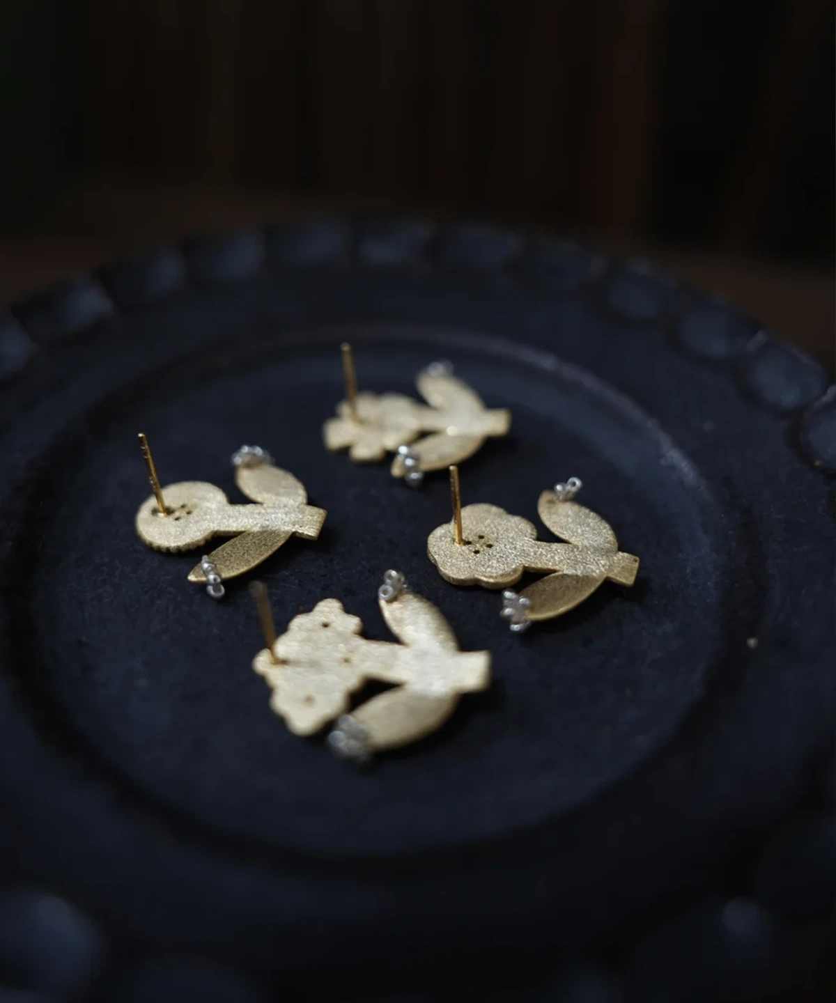 Backs of four gold flower stud earrings on a black ceramic plate, posts showing