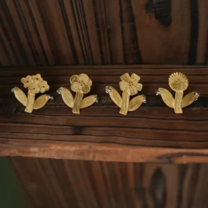 Four gold flower earrings designs standing in a row on dark wood