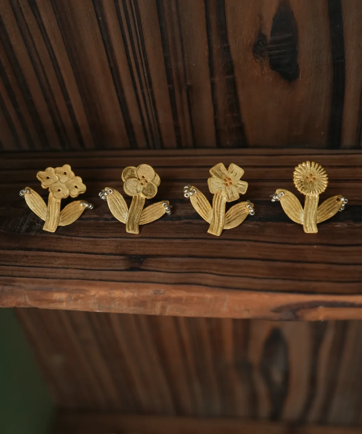 Four gold flower earrings designs standing in a row on dark wood