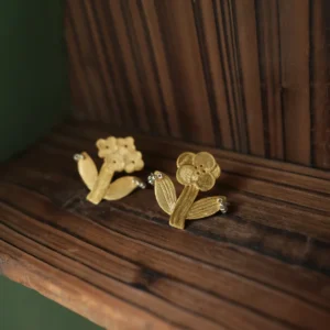 Two gold flower earrings on dark wood — a bloom cluster and a round-petal flower
