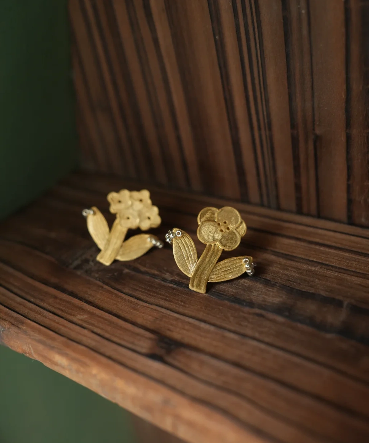 Two gold flower earrings on dark wood — a bloom cluster and a round-petal flower
